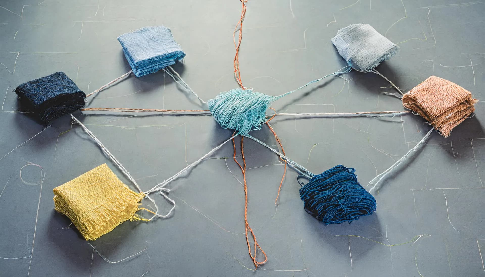 Folded fabric swatches in yellow, navy, light blue, gray, and copper, linked by threads to a tangled ball of turquoise yarn in the center like a network